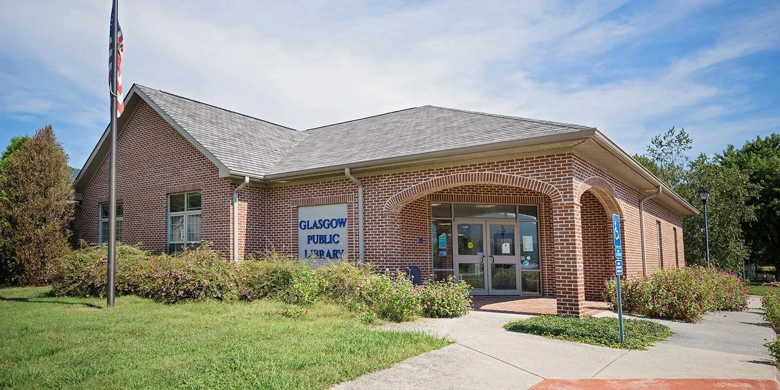 The Glasgow branch of the Rockbridge Regional Library — a long brick building with a peaked metal roof and an American flag out front.